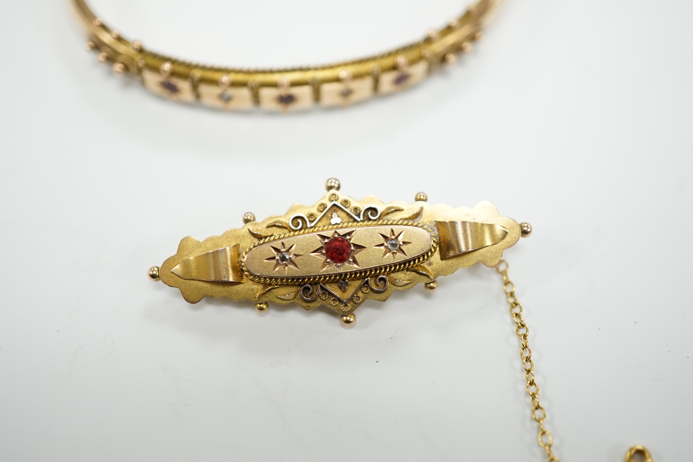 An Edwardian 9ct gold ruby and diamond chip set hinged bangle and a similar yellow metal, ruby and diamond chip set bar brooch, gross weight 12.1 grams.